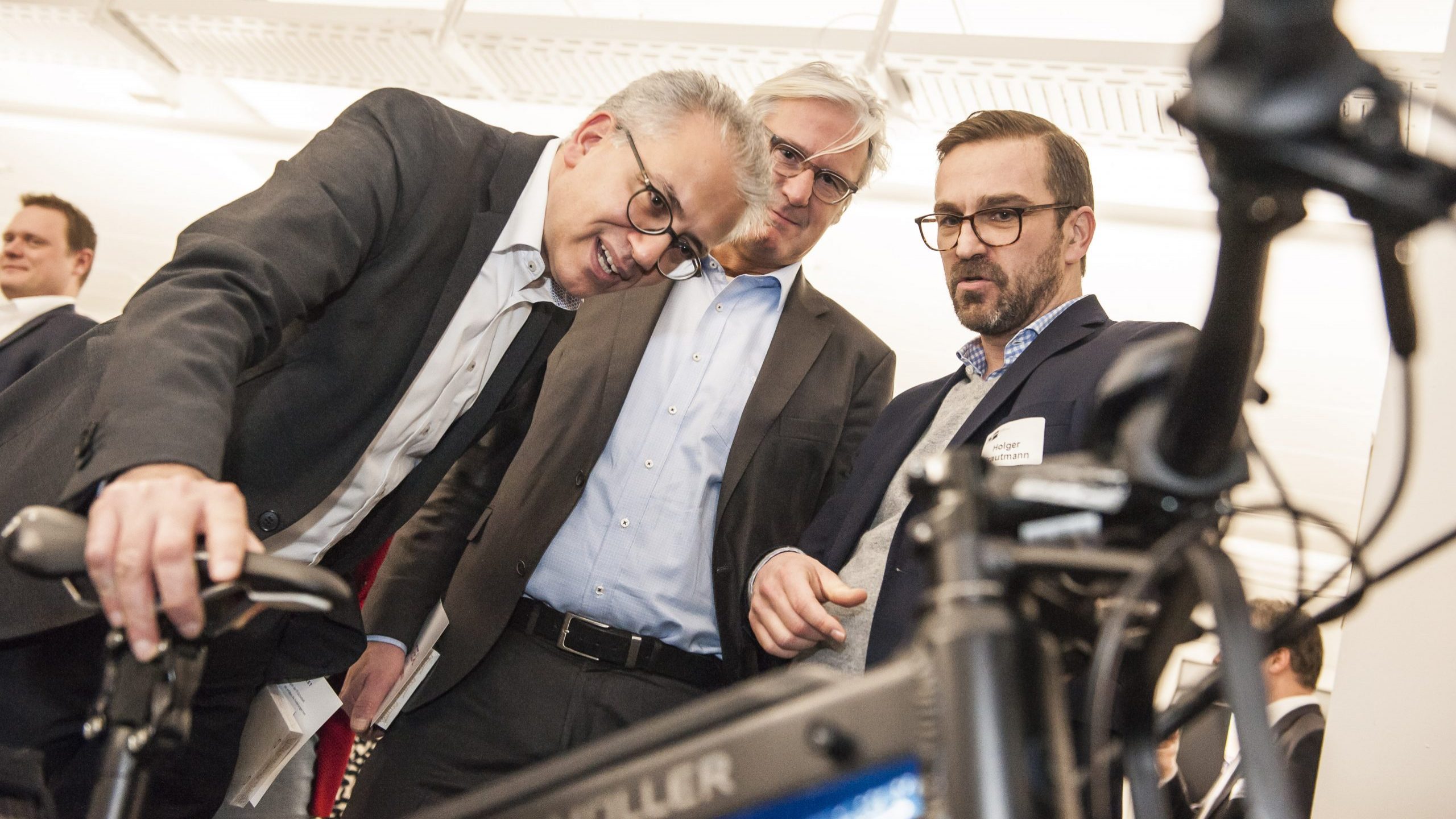 Ein Foto von drei Männern, rechts ein Mitarbeiter von uns. Schauen sich ein Schwarzes E-Bike von Riese und Müller an.