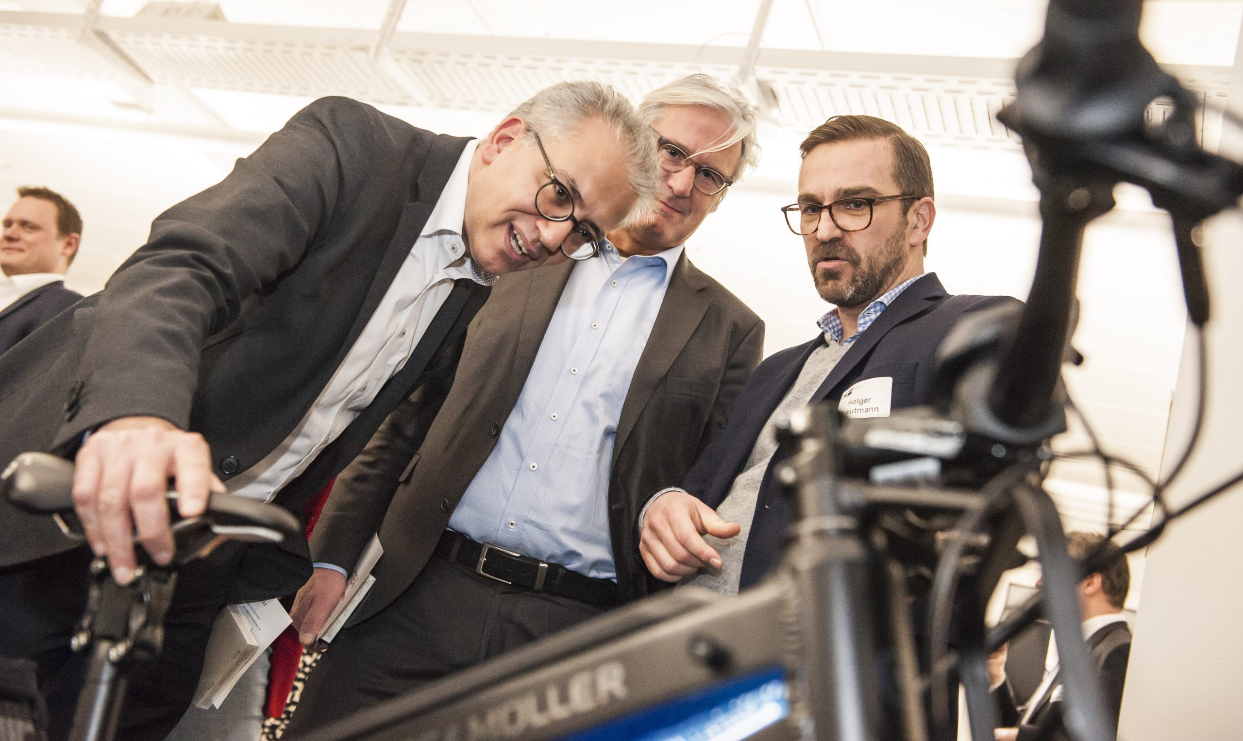 Ein Foto von drei Männern, rechts ein Mitarbeiter von uns. Schauen sich ein Schwarzes E-Bike von Riese und Müller an.