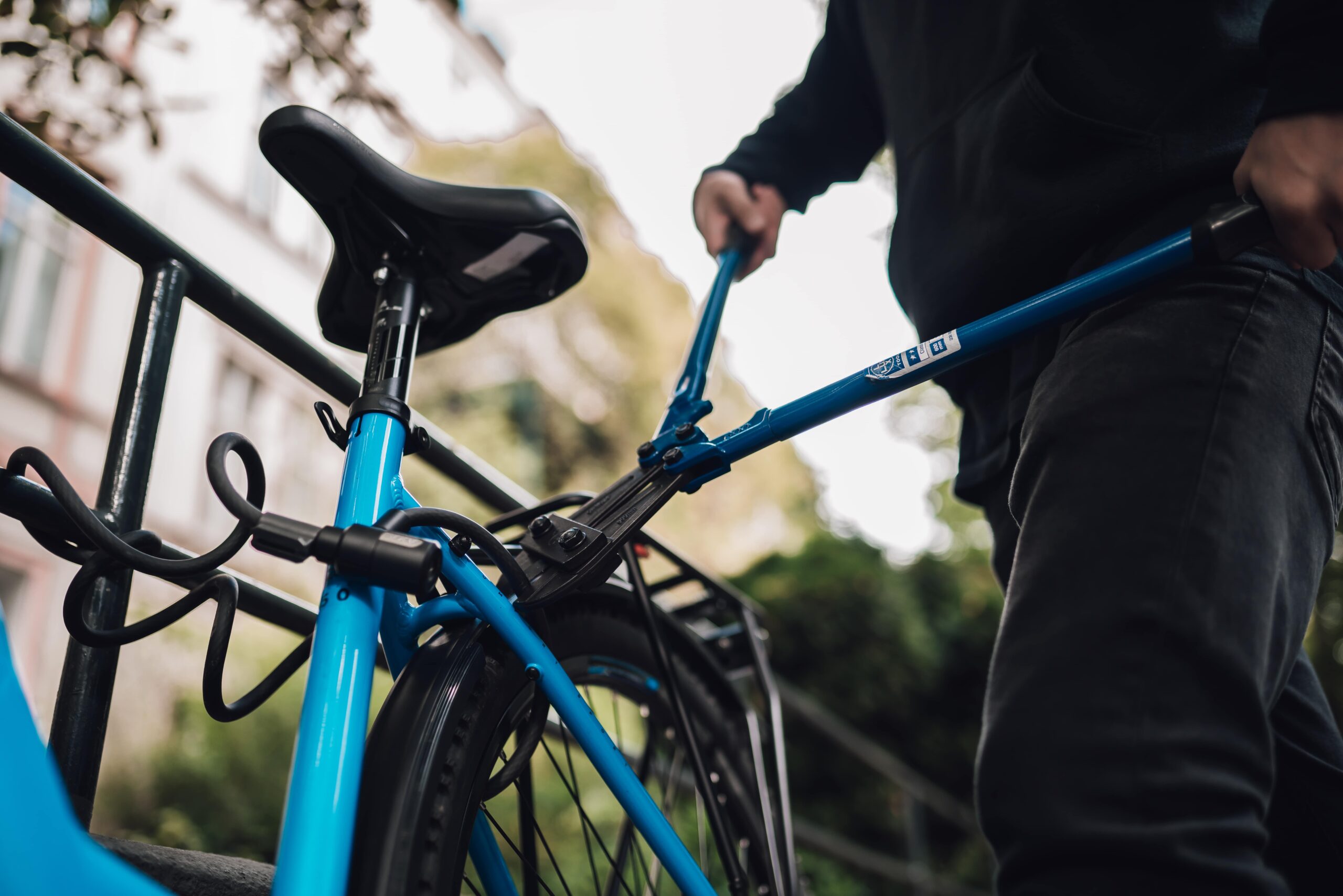 Blaues Bike mit Schloss. Rechts ein Dieb mit Bolzenschneider, schneidet Schloss durch.